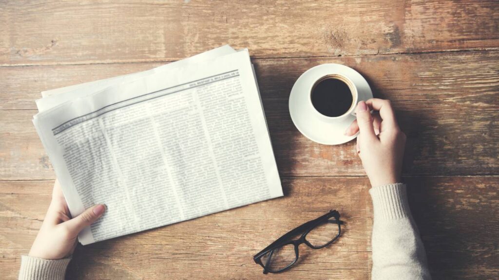 krant op tafel met hand die koffiebeker vastpakt